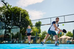 Young man playing padel in Cyprus on a blue outdoor court with partner in the background.
