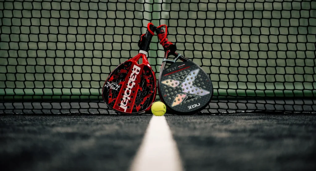 Δύο ρακέτες padel και μία μπάλα μπροστά από το φιλέ, σε κλειστό γήπεδο padel στην Κύπρο